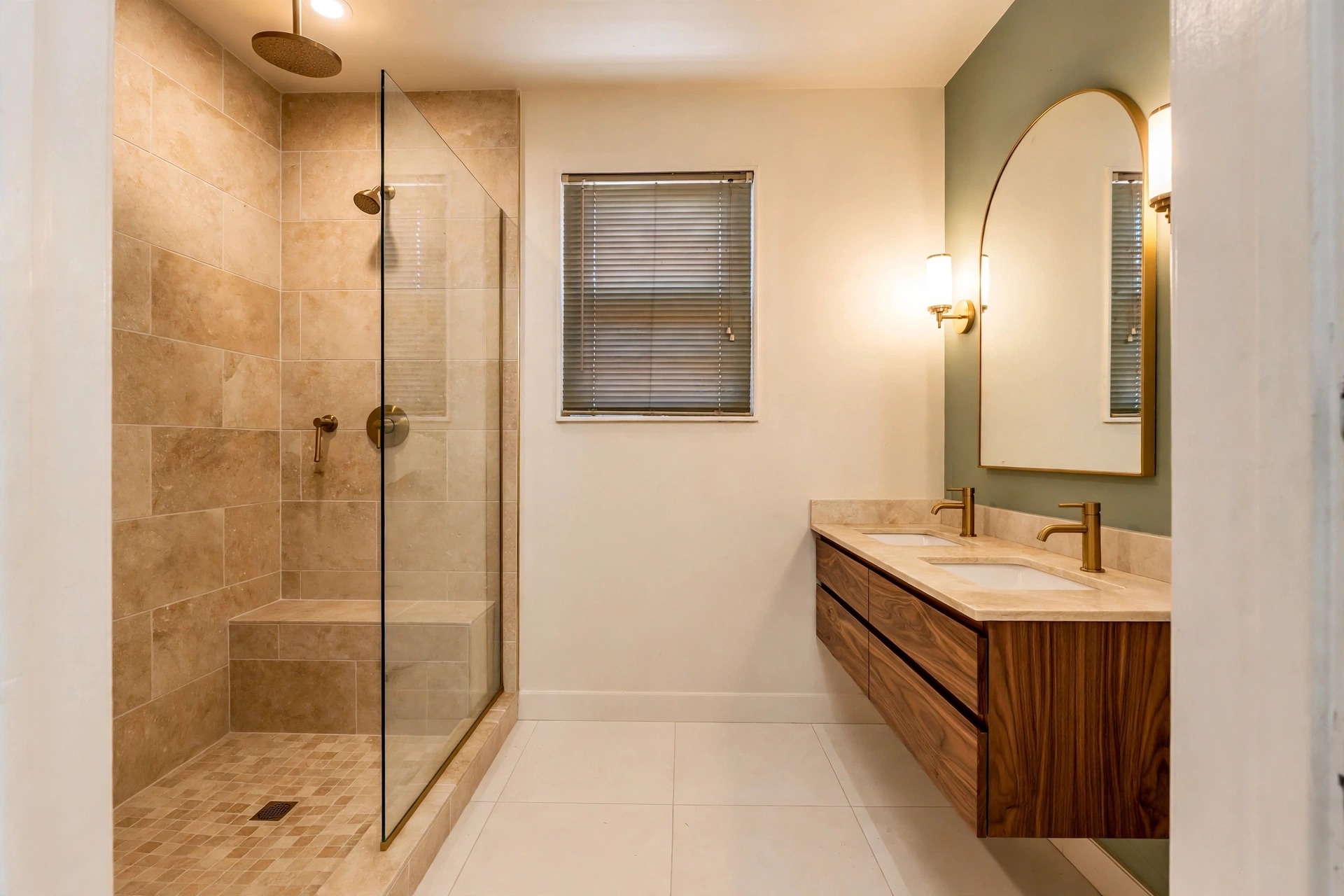 After: the same bathroom redesigned — walk-in travertine tile shower with glass panel, walnut double vanity, brushed brass faucets and a sage green accent wall