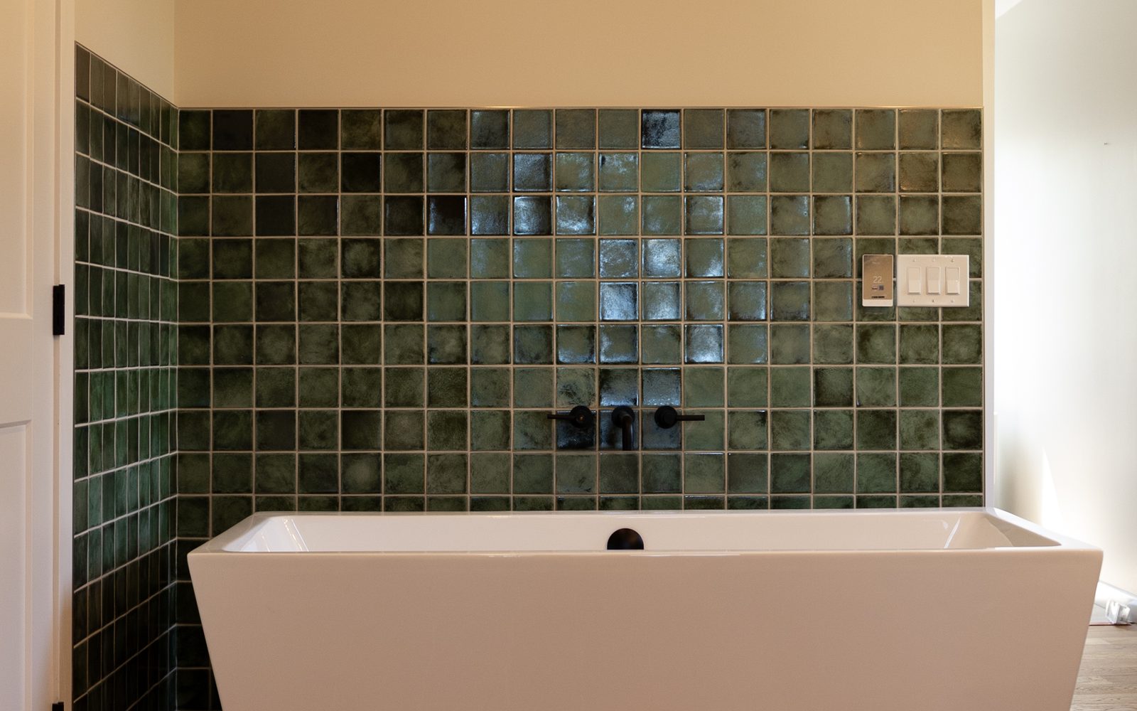 Finished ensuite built by Lions Group: freestanding tub against a deep green zellige tile wall with matte black wall-mounted faucets