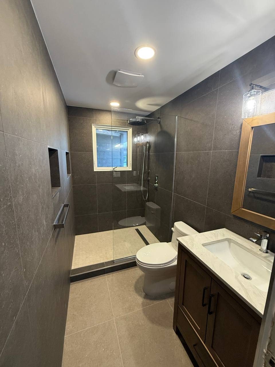 Finished bathroom by Lions Group: glass shower, wood vanity and large-format brown stone tile