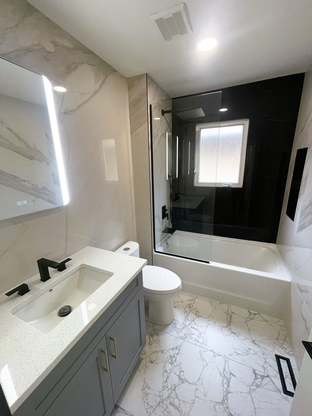 Finished bathroom by Lions Group: marble-look tile, grey vanity and black glass tub enclosure